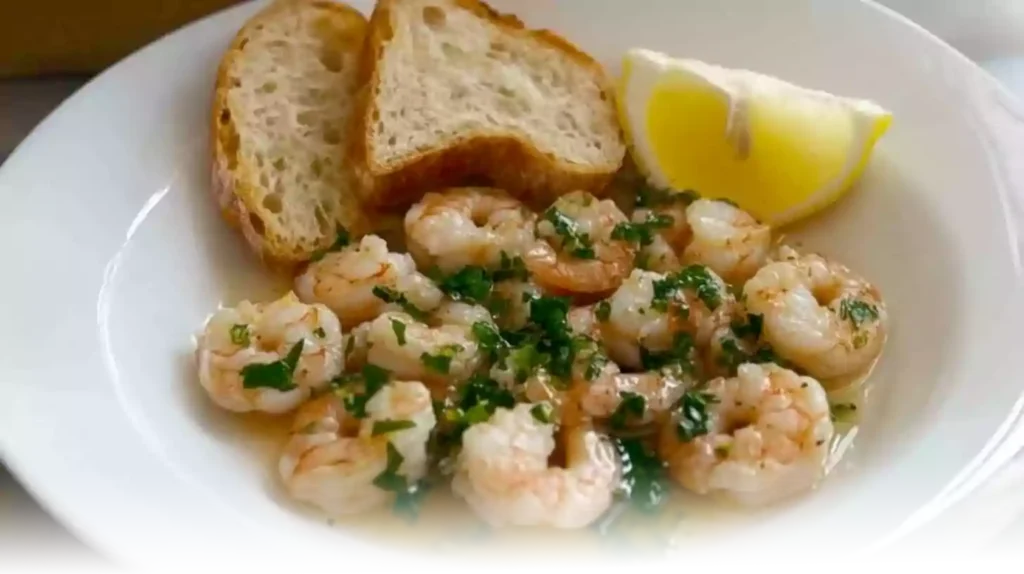 A close-up of shrimp cooking in a skillet with garlic and butter sauce, surrounded by seasonings and ingredients.