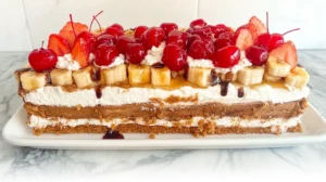 A classic banana split cake, beautifully layered with fruits and cream, garnished with cherries and chocolate drizzle.