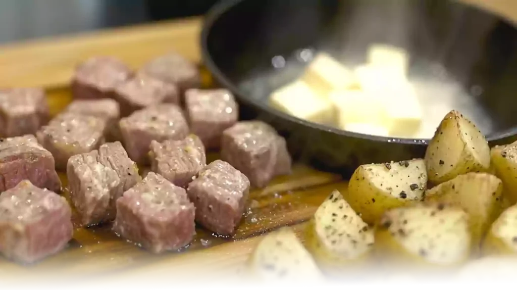 Cooking steak bites in a cast iron skillet, with crispy potatoes on the side and garlic butter sauce being prepared.