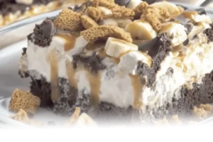 Golden Banana Pudding Brownies with distinct layers of chocolate brownie, pudding, and wafer crumble, garnished with caramel and whipped cream.