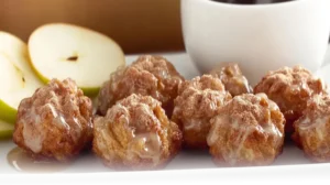 Golden-brown baked apple fritters with a glaze, served on a white plate in a bright modern kitchen.