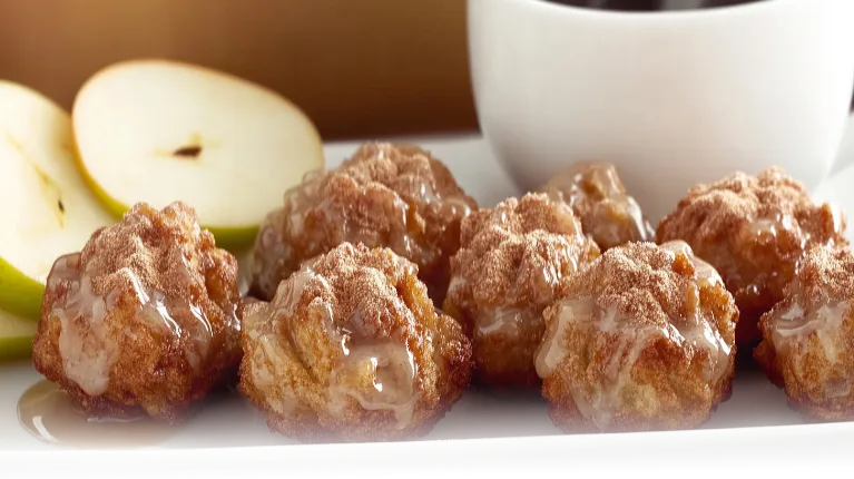 Golden-brown baked apple fritters with a glaze, served on a white plate in a bright modern kitchen.