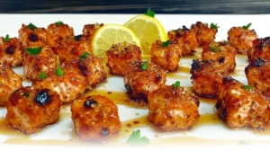 Perfectly caramelized Honey Butter Garlic Salmon Bites served on a white plate, garnished with parsley and lemon zest.