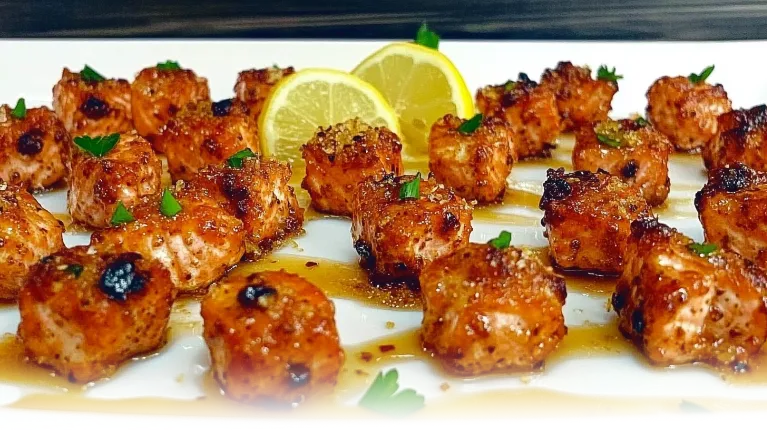 Perfectly caramelized Honey Butter Garlic Salmon Bites served on a white plate, garnished with parsley and lemon zest.