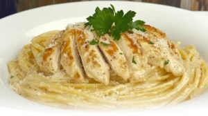 A bowl of Creamy Garlic Parmesan Chicken Pasta with golden chicken slices, garnished with parsley and parmesan cheese.